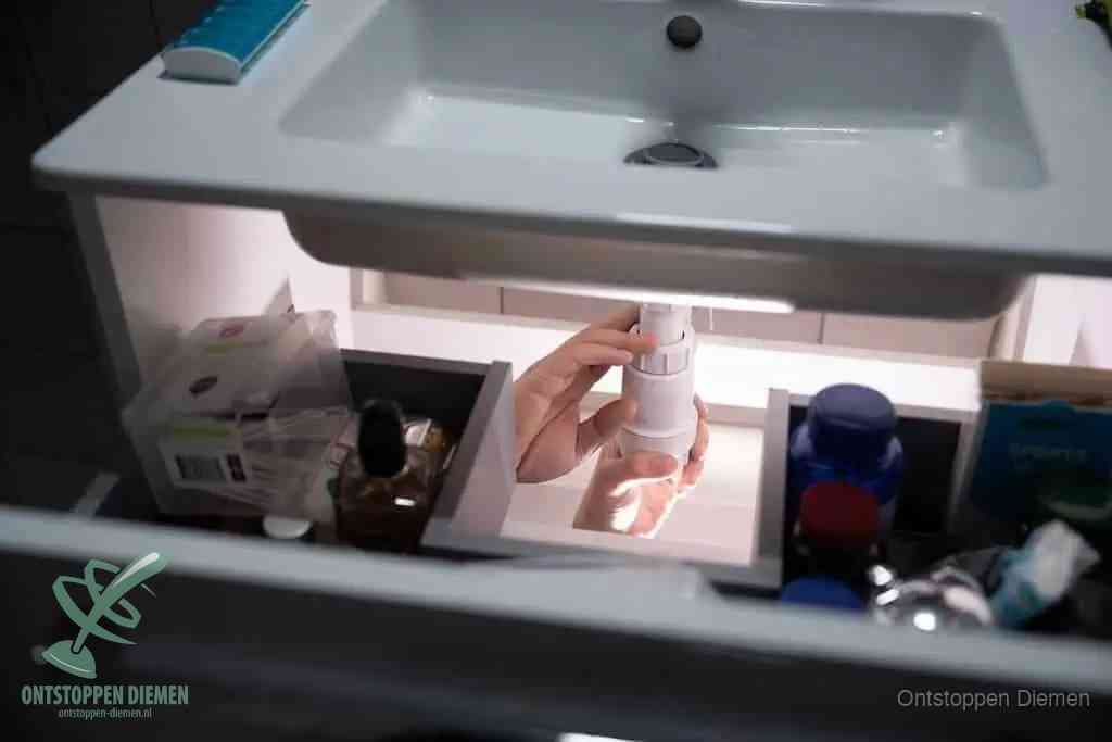 Een pompfles met zeep boven een wastafel, de heet water en afwasmiddel-methode om een vetprop in de afvoer los te maken in Diemen