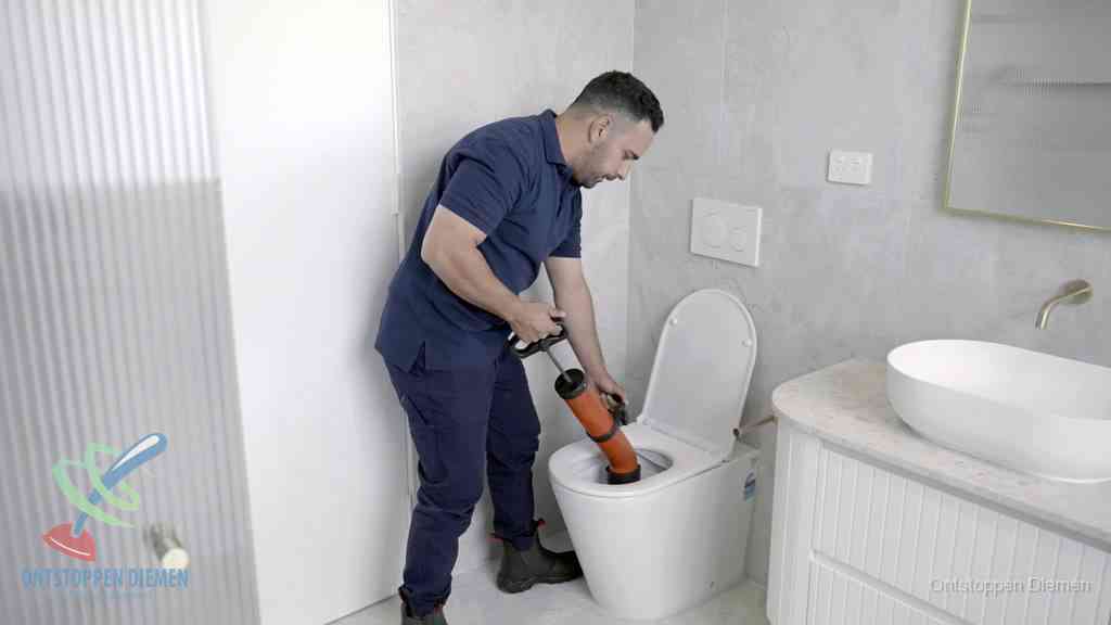 Een monteur buigt over een wandcloset en duwt met de hand een persluchtontstopper in de toiletpot om de verstopping handmatig los te maken in Diemen
