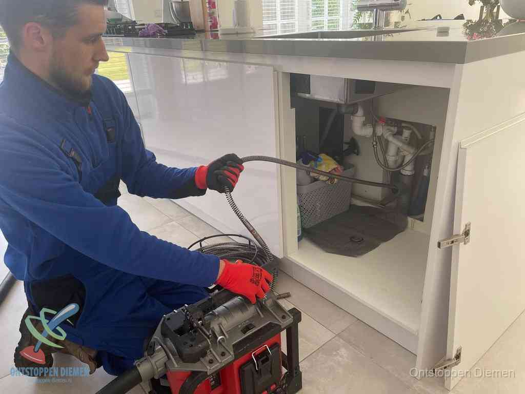Monteur voert een ontstoppingsveer in de afvoer onder de keuken in Diemen