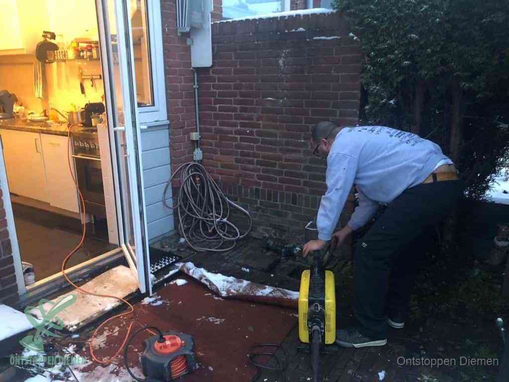 Een monteur werkt buiten bij een open riool-/grondput met een elektrische ontstoppingsmachine om een verborgen afvoerprobleem op te sporen in Diemen