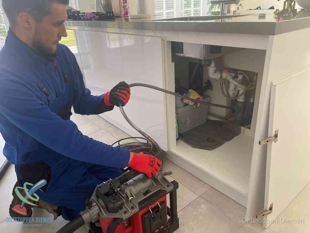 Een monteur reinigt de keukenafvoer grondig met een veermachine om terugkerende gootsteenverstoppingen te voorkomen in Diemen