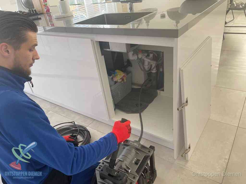 Monteur ontstopt met een veermachine een verstopte afvoer onder de gootsteen in Diemen