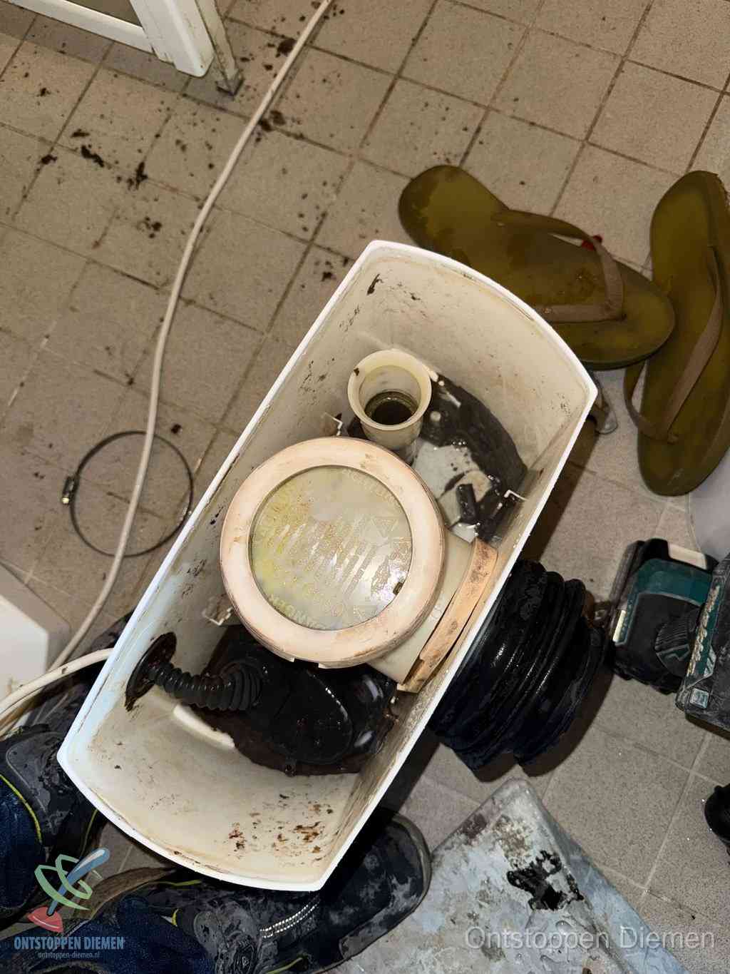 Een gedemonteerde toiletpot op de vloer met ontstoppingsveer en gereedschap ernaast, het verwijderen van een vastzittend voorwerp uit de wc in Diemen