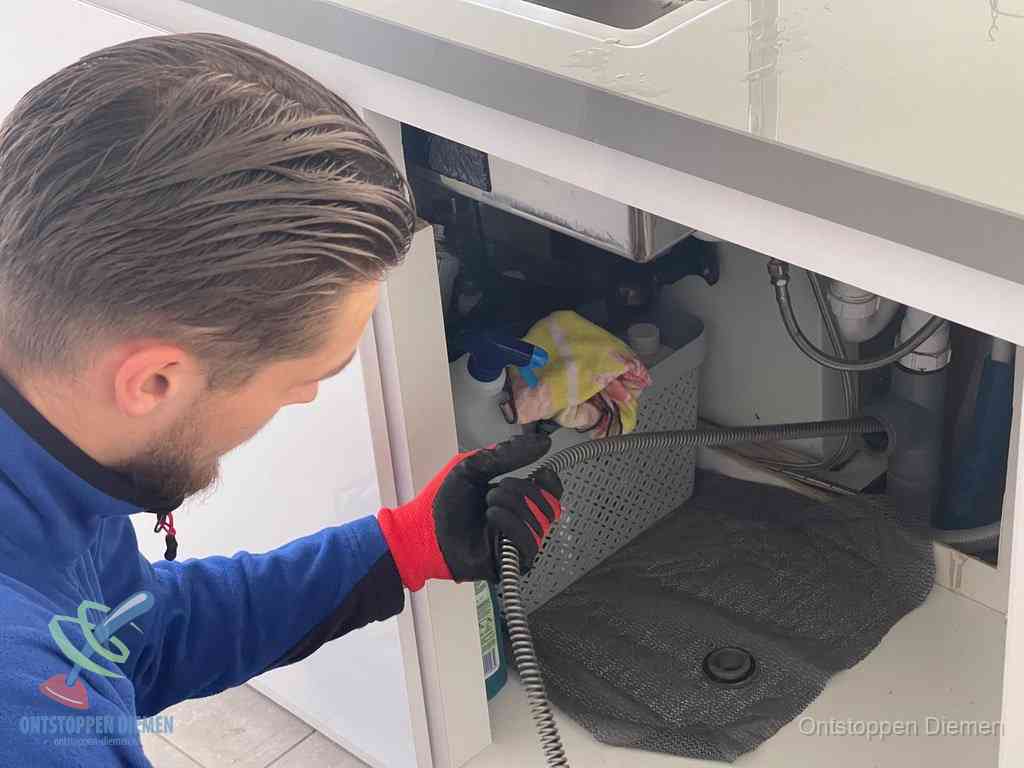 Een monteur voert een flexibele ontstoppingsveer in de afvoer om een verstopping voorbij de bocht van het toilet te bereiken in Diemen