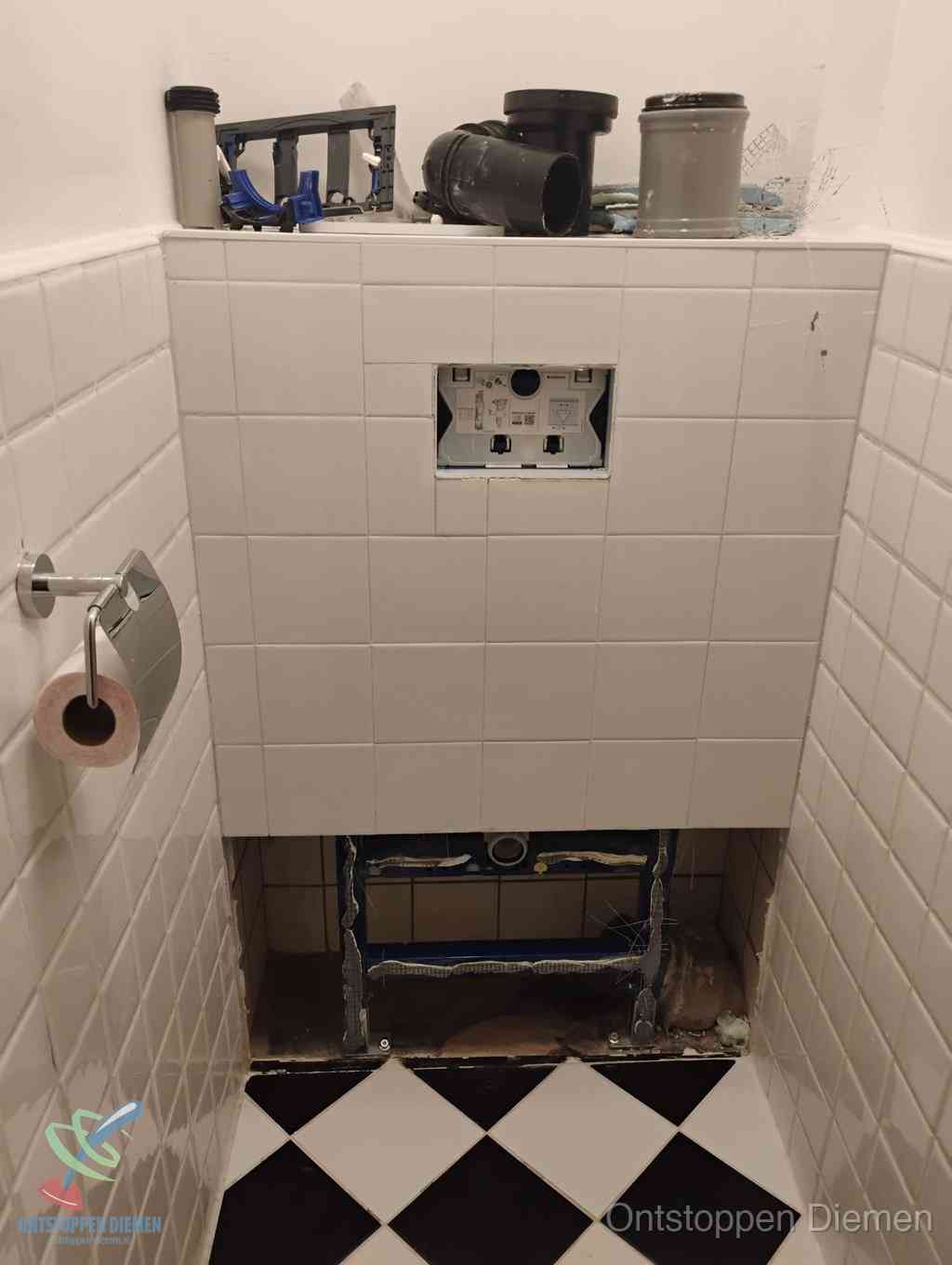 Een toiletruimte waar het hangtoilet en de inbouwreservoir-onderdelen zijn vrijgelegd voor onderhoud, periodiek nazicht voorkomt een wc-verstopping in Diemen