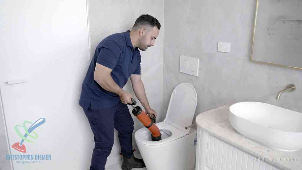 Een monteur gebruikt een handmatige perspomp (toiletontstopper) op een wandcloset tijdens het professioneel wc ontstoppen in Diemen