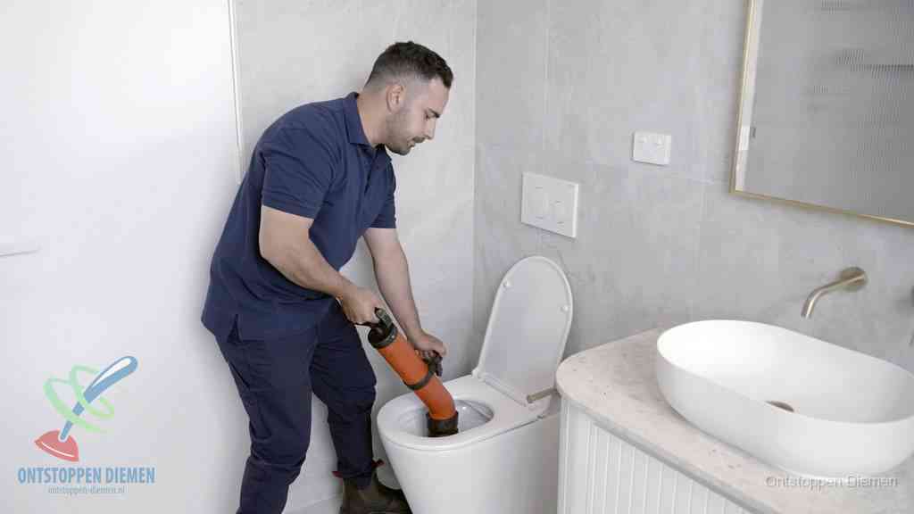Een man gebruikt een handmatige luchtdruk-ontstopper in een modern betegeld toilet om zelf de wc te ontstoppen in Diemen